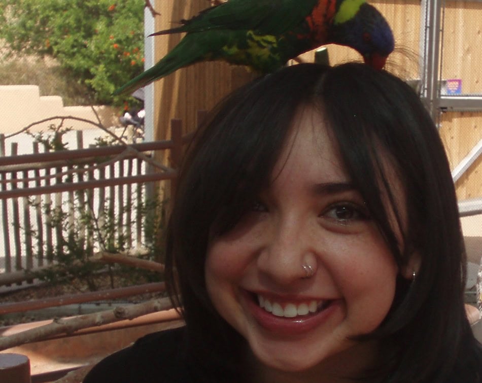 Brynn Mora smiling at the camera while a colorful parrot sits atop her head.
