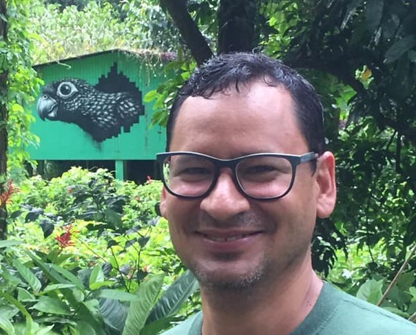 Brian Ramos Guivas smiling at the camera. He is wearing black-framed glasses and a medium-dark green shirt.