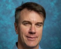 Headshot of Timothy Wright. He is wearing a blue shirt in front of a blue background and is smiling.