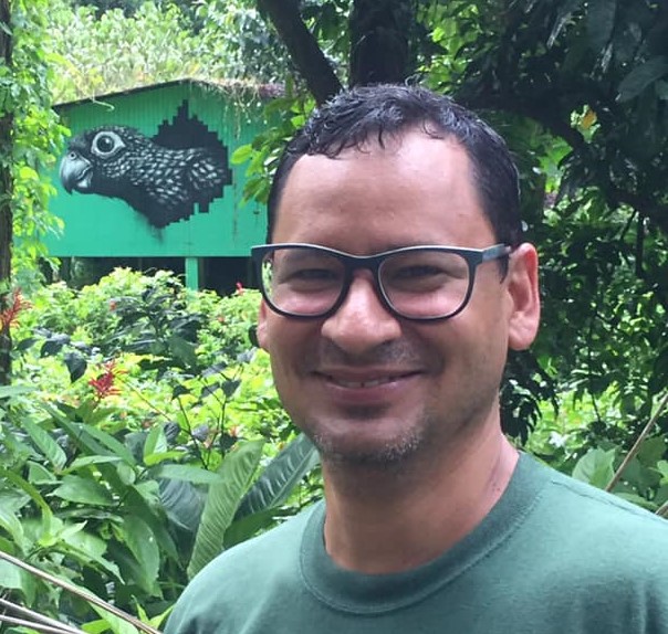 Brian Ramos Guivas smiling at the camera. He is wearing black-framed glasses and a medium-dark green shirt.